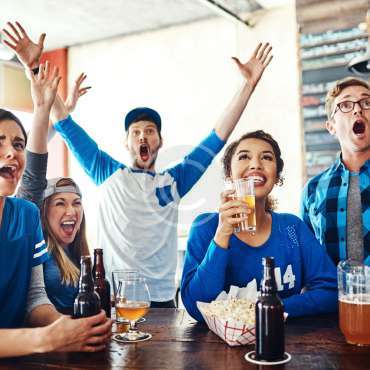 Shot of a group of friends cheering while watching a sports game at a bar